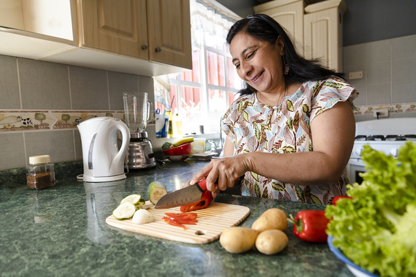 Ama de casa cortando cebolla, pepino y pimiento mientras sonríe